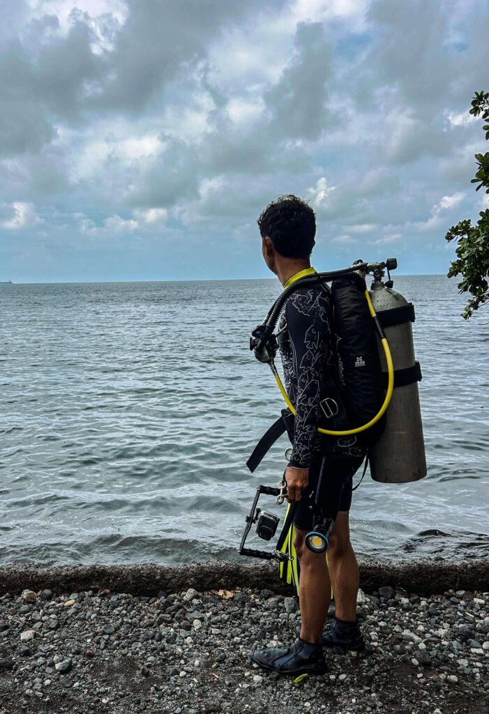 An underwater photographer standing by the ocean with an underwater camera in his hands